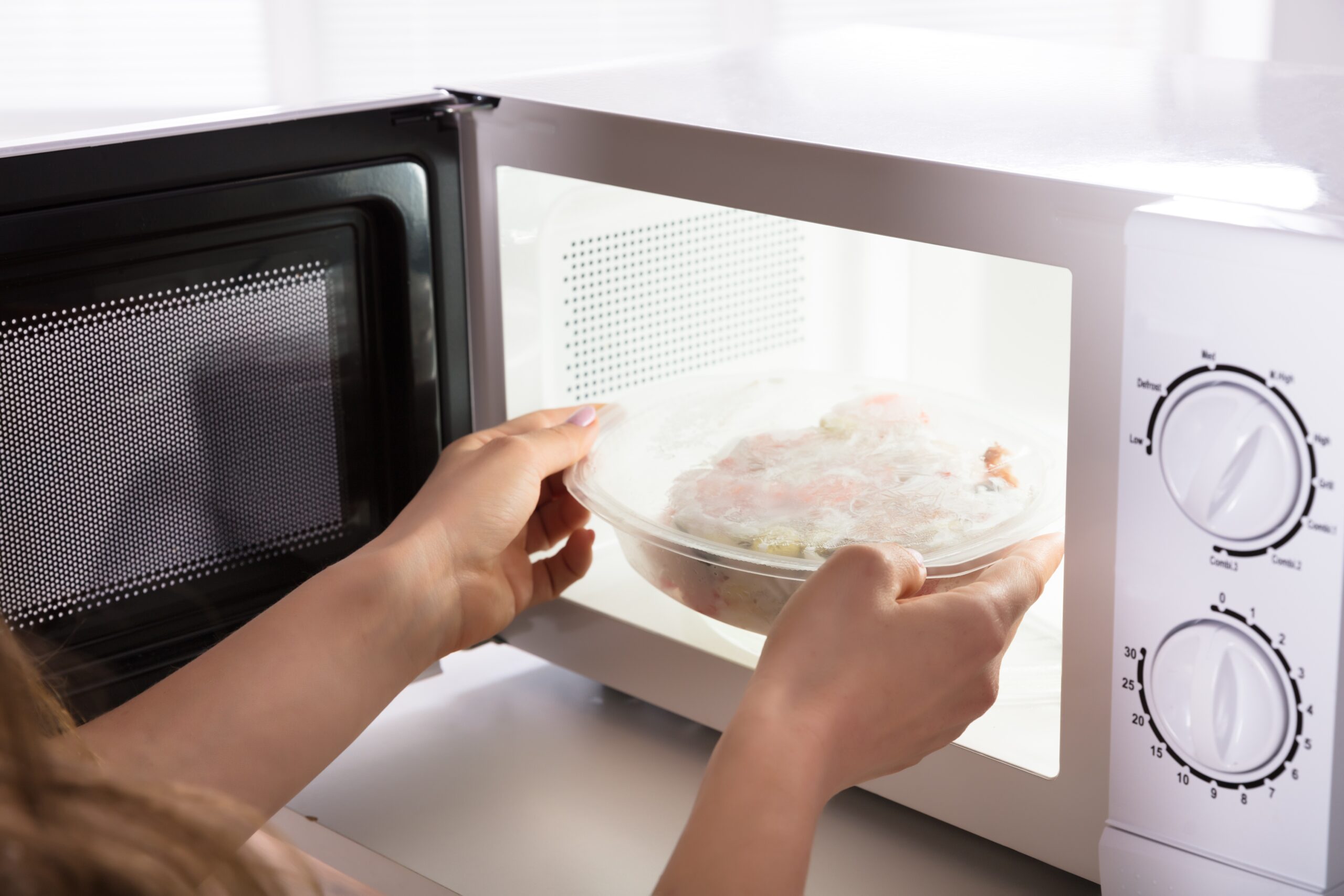 Close-up Of A Woman's Hand Heating Food In Microwave Oven